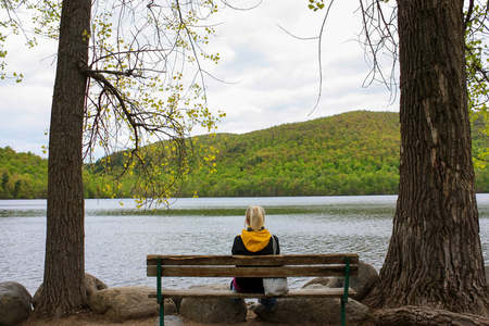 young girl sitting on a bench looking at a lakeの写真素材
