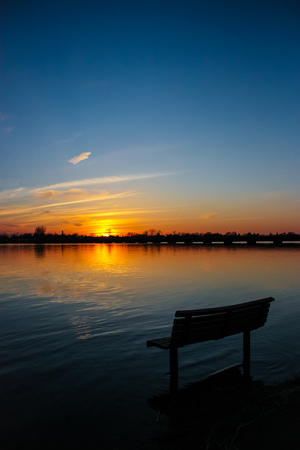 bench on the side of a river with a sunsetの写真素材