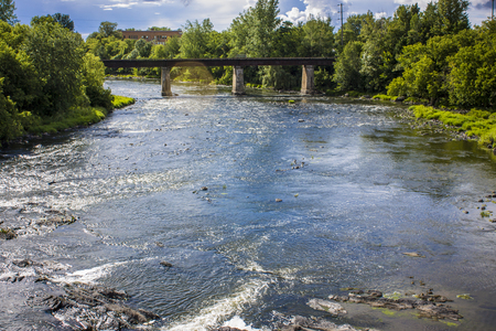 river with rocks flowing under a train bridgeの写真素材