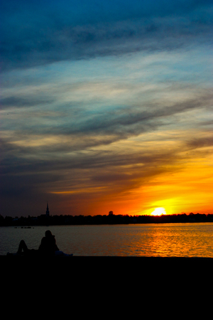two people sitting by the water at sunsetの写真素材