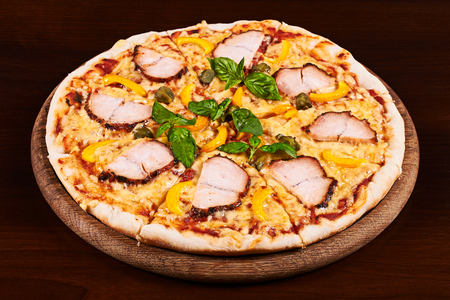 Chicken pastrami, yellow pepper and capers pizza on a wooden tableの写真素材