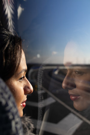 Latina woman on a bus looking out the window, smiling and her face reflected in the glass.の写真素材