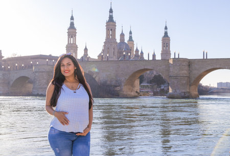 Pregnant latin woman in the cathedral of Pilar next to the Ebro river and the bridge of Priedra, wearing blue clothes and sunglasses.の写真素材