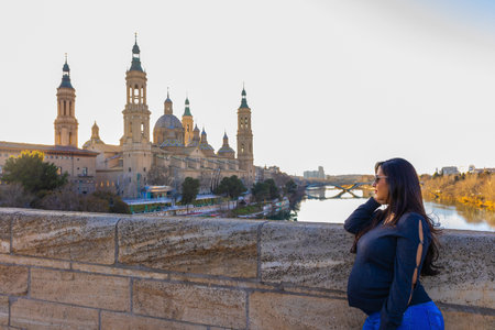 Pregnant young woman looking at the Pilar Cathedral from the stone bridge in Zaragoza, Spain.の写真素材