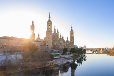 Panoramic view of the Pilar Cathedral and the Ebro river, with the sunset on the left side, blue sky and reflection on the water.の写真素材