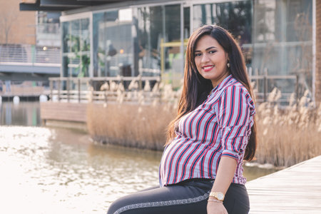 Young pregnant woman sitting on a dock, smiling and looking at the camera.の写真素材