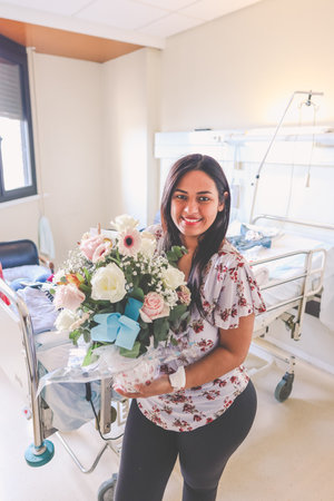 Woman smiling in a hospital room with a bouquet of flowers in her handsの写真素材