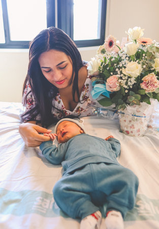 Mother looking at her newborn baby in a hospital bed and a bouquet of flowers at her bedsideの写真素材