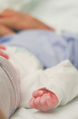 Newborn baby's hand held while sleeping in hospital bedの写真素材