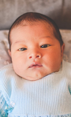 newborn baby, lying down, looking at the camera and wearing blue clothing
