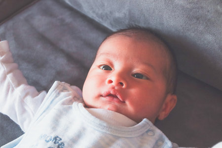 Newborn lying on a gray sofa with open arms, smiling and wearing white clothes.の写真素材