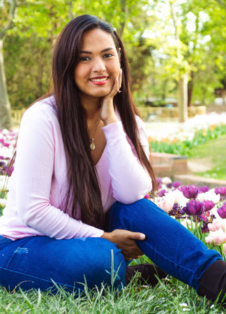 Beautiful young woman, smiling and sitting in a city park with purple tulips.の写真素材