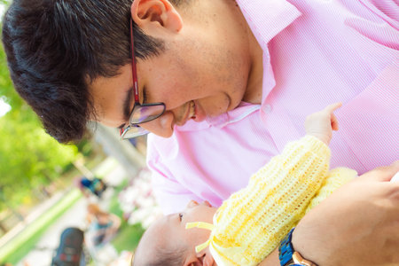 Latin dad sipping and looking at his newborn baby in the parkの写真素材