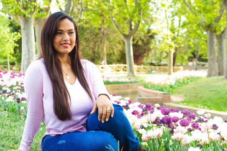 Latin woman, smiling and looking at the horizon in a city park, with tulips and greenery in the background.の写真素材