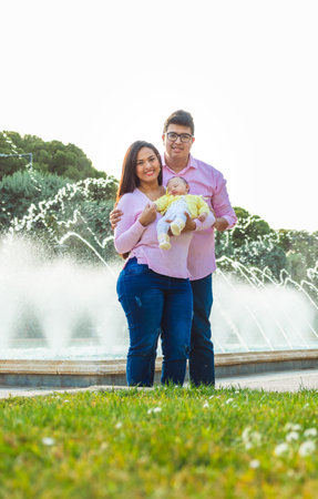 Straight couple with their newborn baby in a park with water fountains in the backgroundの写真素材