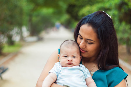 Young mother looking tenderly at her newborn baby, walking in a park.の写真素材
