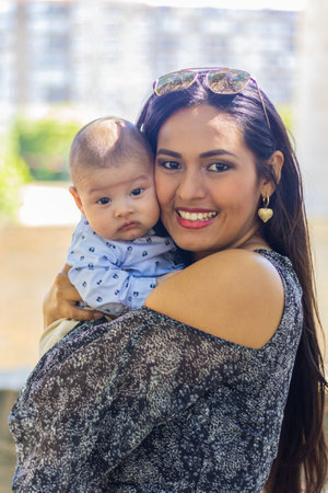 Happy mom hugging her baby in a park, smiling and looking at the camera.の写真素材