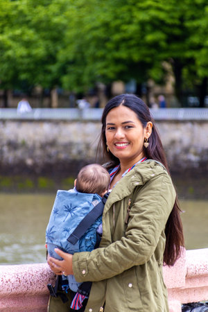 Woman with baby in a blue baby carrier on a city bridgeの写真素材