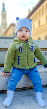 Beautiful baby sitting on a city stairwell in winterの写真素材