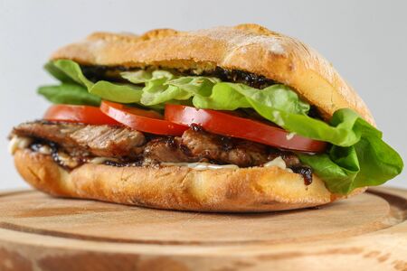 Tasty pork steak sandwich in a ciabatta with tomatos, lettuce, mayonnaise and barbecue sauceの写真素材