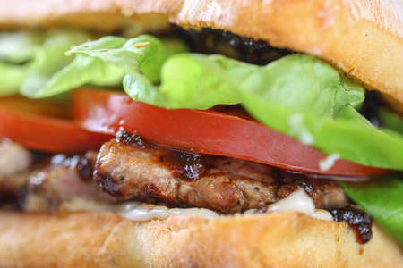 Tasty pork steak sandwich in a ciabatta with tomatos, lettuce, mayonnaise and barbecue sauceの写真素材