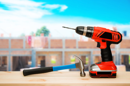 Hammer and cordless driller on wooden desk. Construction site as background.の写真素材