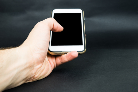Hand hold white mobile phone, cellphone with black blank screen on dark backgroundの写真素材