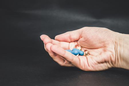 Hand hold pill or tablet, try to reach the pill. Dark background. Blue, orange tablet.の写真素材