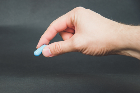 Hand hold pill or tablet, try to reach the pill. Dark background. Blue, orange tablet.の写真素材