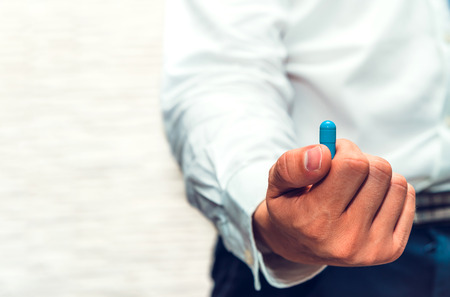 Hand holds blue pill. Businessman holding a pill in front of the camera