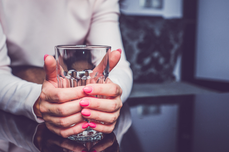 Holding an empty glass in hands. A woman is holding her hands on a table, squeezing an empty glass. Waiting for drink, conversation, waiting for something, concept.の写真素材