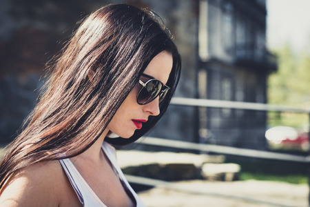 Portrait of a beautiful and cute girl with sunglasses. Close-up of the face of a woman looking down, focused. The sun's rays illuminate the hair of the female. Concept lifestyle outside.の写真素材