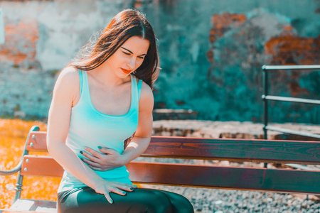 The woman is holding her belly. The girl is suffering, her stomach hurts. Abdominal pain during a seat on a park bench. Female problems.の写真素材
