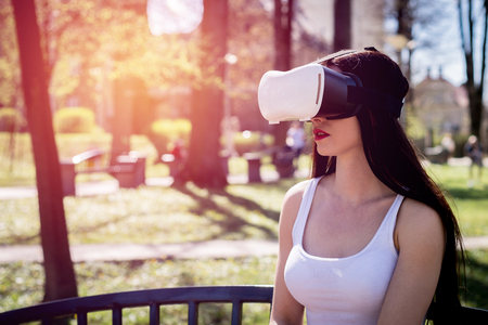 Virtual reality, fun in the park. A woman relaxes in the park using VR. The girl imagines that she is climbing the rope. Spending free time outside, lifestyle concept.の写真素材