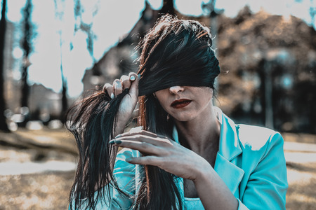 A nostalgic portrait of women sitting on a bench and covering her face with her hair. Invisible eyes. A thoughtful and serious woman looks ahead.の写真素材