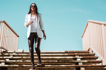 A woman wearing a blue jacket and sunglasses runs down the stairs.の写真素材
