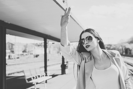 Vintage look at a woman calling friends. The woman on the platform raises her hand calling someone. A beautiful and attractive woman is wearing sunglasses. Travel concept, expectations.の写真素材