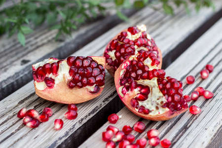 Juicy pomegranate fruit and red flower over wooden tableの写真素材