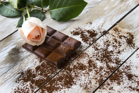 Turkish coffee with peach-colored rose and slices of chocolate on the wooden table