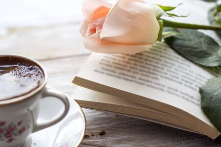 Turkish coffee with peach-colored rose, slices of chocolate and book on the wooden tableの写真素材