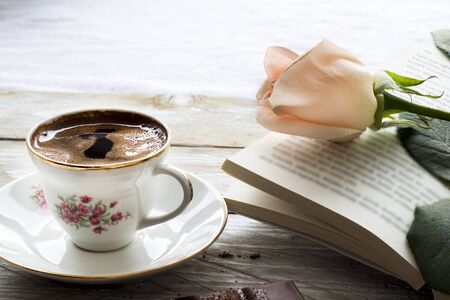 Turkish coffee with peach-colored rose, slices of chocolate and book on the wooden tableの写真素材