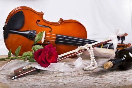 Violin, red rose, pearl necklace and wine on wooden tableの写真素材