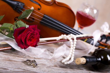 Violin, red rose, pearl necklace and wine on wooden tableの写真素材