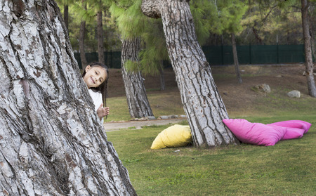 Happy little girl hiding behind the tree on green grassの写真素材