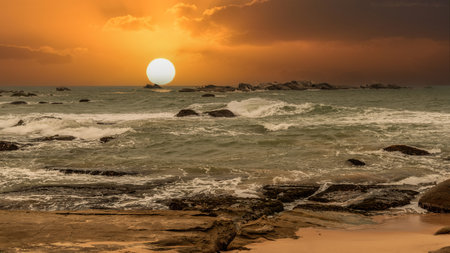 beautiful sunset over the ocean with rocks in the foregroundの写真素材