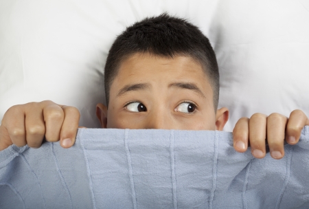 Scared boy hiding in bedの写真素材