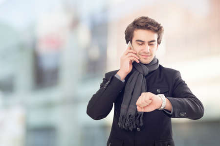 Young businessman talking on mobile phone and  looking at watch on street