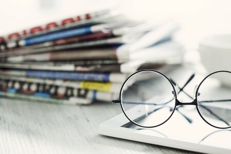 Stack of newspapers, eyeglasses and digital tablet