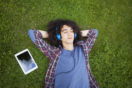 Young man lying on grass and listening musicの写真素材