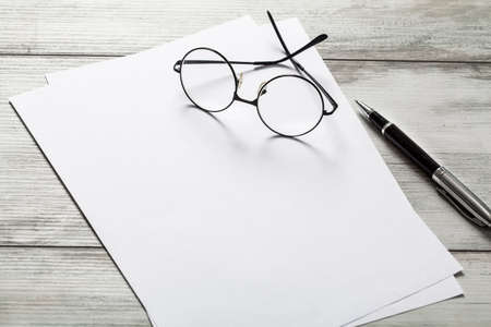 White page with pen and eyeglasses on tableの写真素材